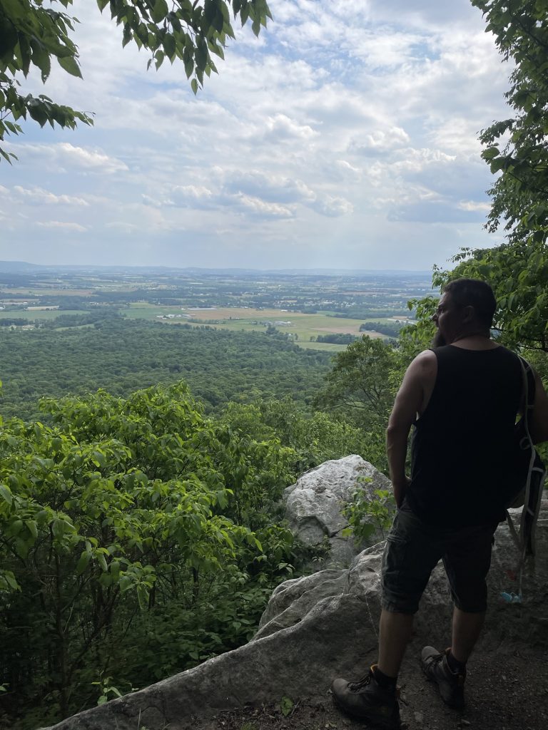 Hiker enjoying a scenic overlook along the Appalachian Trail with views of Pennsylvania farmland and forests below